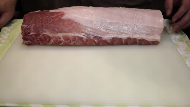 Close-up of pork loin being sliced using a knife on a cutting board in a kitchen.