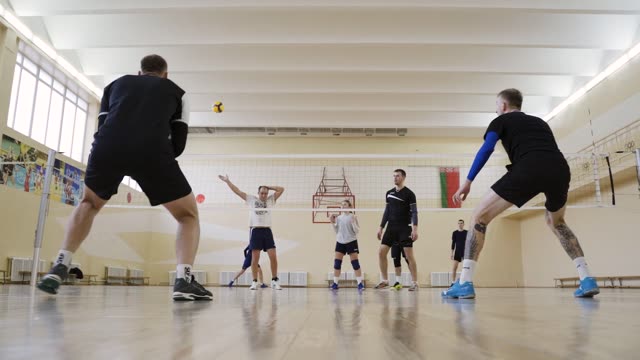 Group of athletes practicing volleyball in a gym.