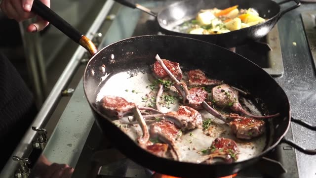 Chef expertly flambés lamb chops in a kitchen setting.