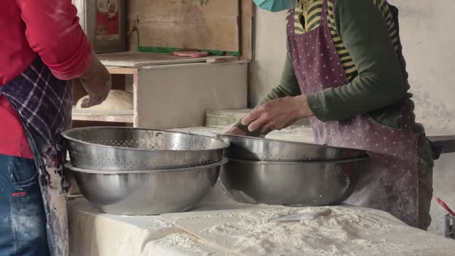 Two adults make dumplings by hand in a cozy kitchen setting.