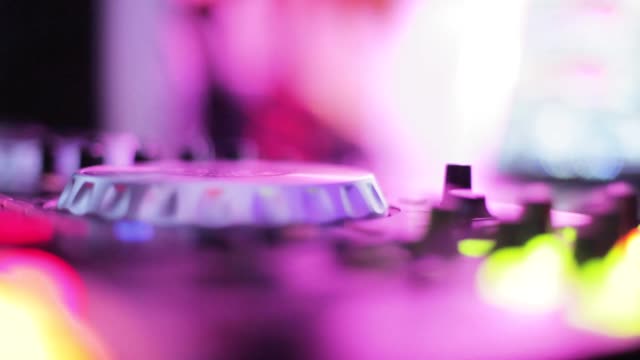 Close-up of DJ mixing music on vibrant neon-lit sound mixer in club.