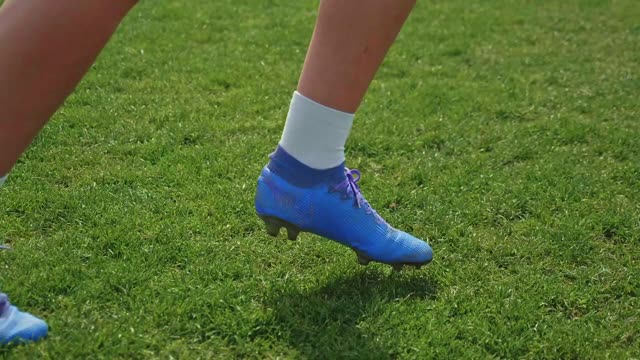 Close-up view of a soccer player wearing blue cleats kicking a ball on grass.