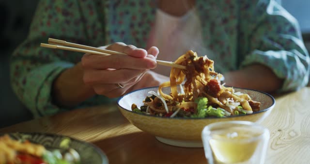A person enjoying delicious noodles with chopsticks in a cozy setting.