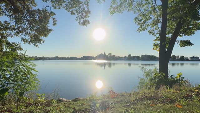 A peaceful sunset over a calm lake with trees and reflections.