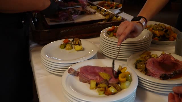 Chef plates steak and roasted vegetables in a restaurant setting.