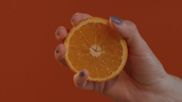 Hand squeezing half an orange to extract juice in slow motion.