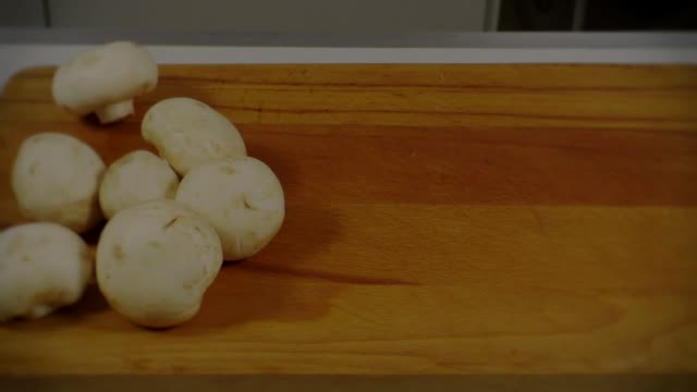 Hands slicing fresh mushrooms on a wooden chopping board in kitchen.