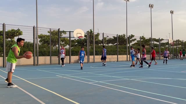 Youth enjoy a friendly basketball game on an outdoor court at sunset.