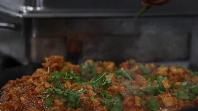 Close-up of spicy Indian dish being prepared with fresh herbs.