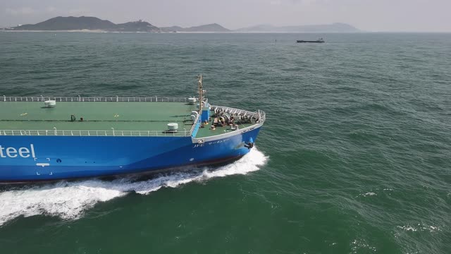 Drone footage of a cargo ship in motion on open water under clear skies.