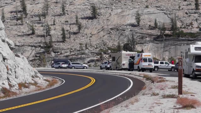 Curved mountain road with parked vehicles under rocky cliffs. Daytime scenery.