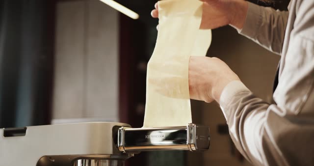 Close-up of hands using a pasta maker to create fresh pasta sheets.