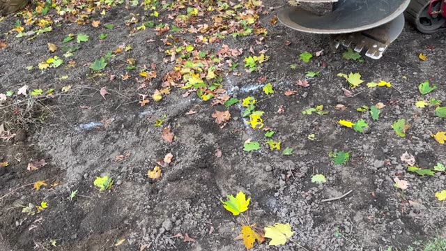 Mechanical excavator digging in a leafy autumn garden. Preparing soil for planting.