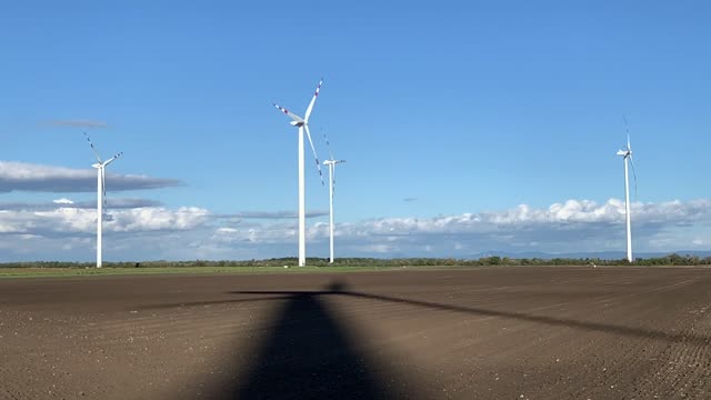 Multiple wind turbines spinning in an open field against a clear blue sky.