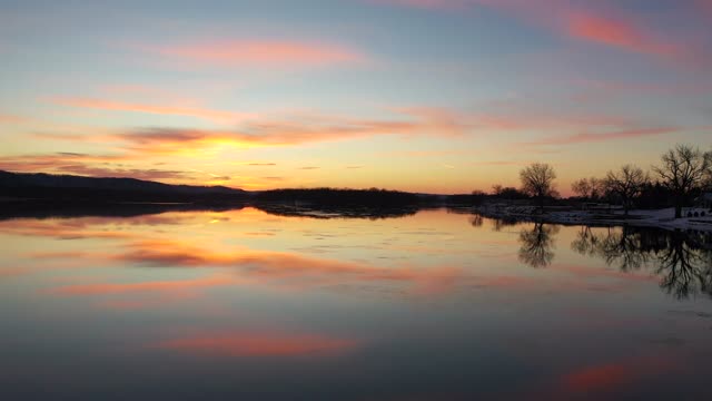 Experience a peaceful winter sunset reflecting over a calm lake.