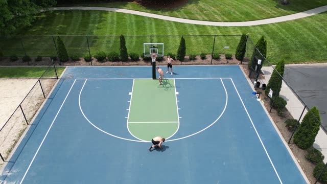 Aerial footage of a basketball game on a sunny day in a park setting.