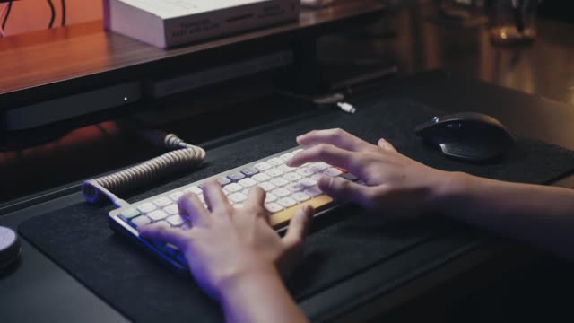 Person typing on a mechanical keyboard in a dimly lit room with computer screen