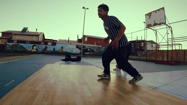 Energetic breakdance routine on an urban basketball court at sunset.