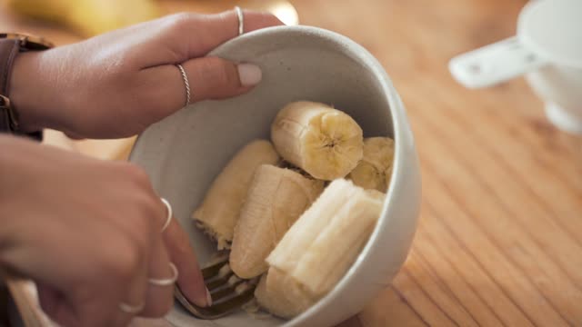Detailed view of hands mashing bananas in a bowl for baking.