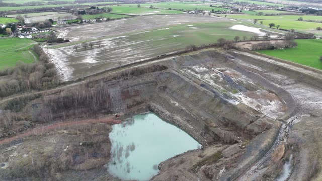 Drone footage capturing a vast, abandoned quarry with water filled pit.