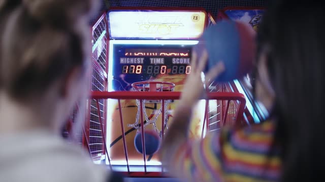 Two girls enjoying a basketball game at an amusement arcade.
