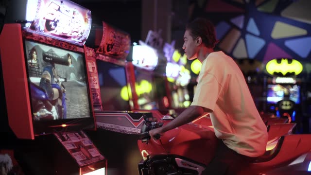 Teen playing an arcade motorcycle game in a vibrant neon-lit setting.