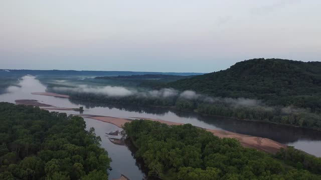 Aerial footage showcasing a misty river winding through a lush, green valley at dawn.