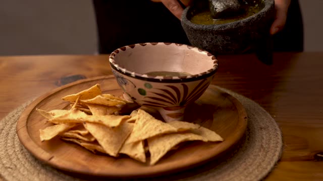 Authentic Mexican salsa being poured into a bowl beside crispy nachos.