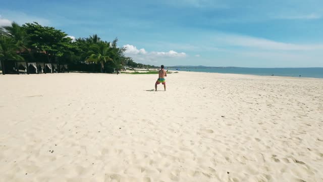A man exercises with a kettlebell on a sunny beach, showcasing fitness training.