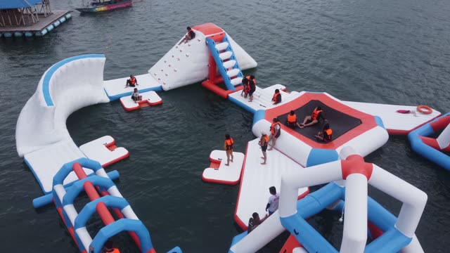 Aerial footage of a fun-filled inflatable waterpark obstacle course on a sunny day.