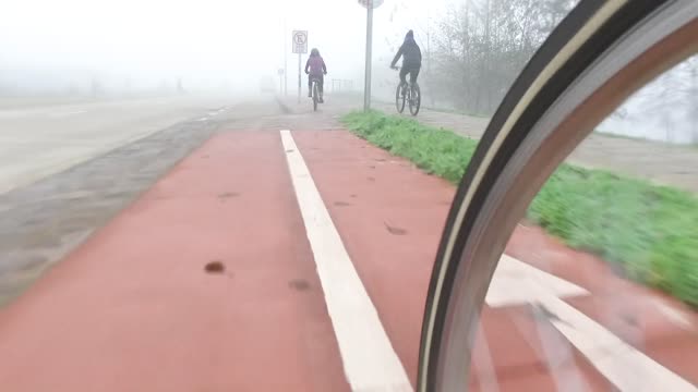 Cyclists ride on a foggy day, creating a serene outdoor experience.