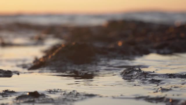 Gentle waves lapping at the shore in slow motion during a stunning sunset.